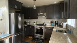 A modern kitchen with dark cabinets, stainless steel appliances, a granite countertop, and a bicycle-themed rug. - University Park Garden Guest House (Portland)
