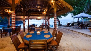 A beachside restaurant with a round table and chairs, thatched roof, and ocean view. - Lumbung Bali Huts (Lembongan Island)