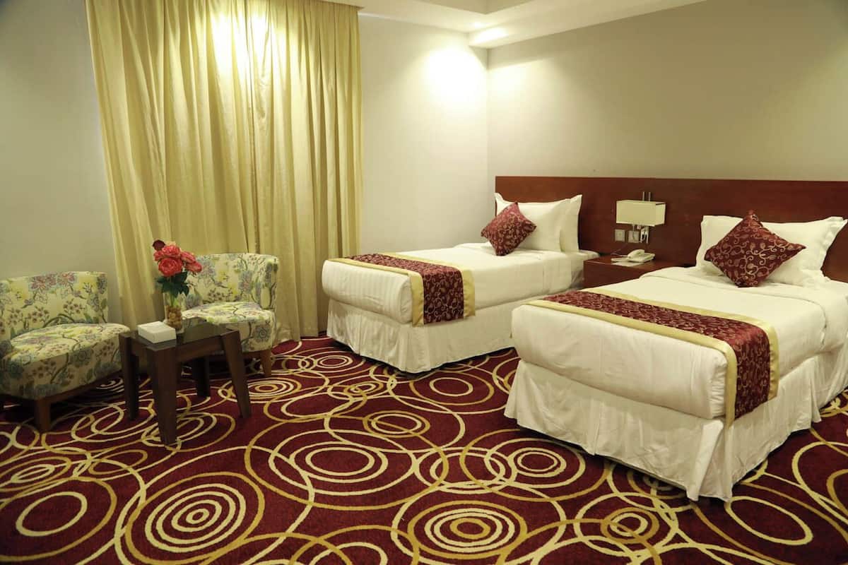 A hotel room with two beds, a small table with a vase of flowers, a sofa, and a patterned carpet.