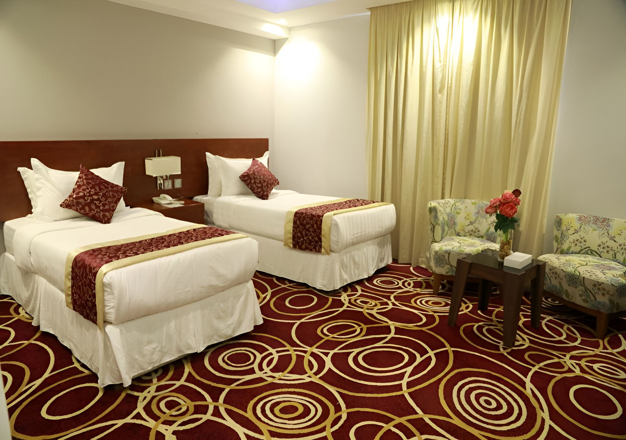 A hotel room with two beds, a desk, a chair, and a large window with curtains.