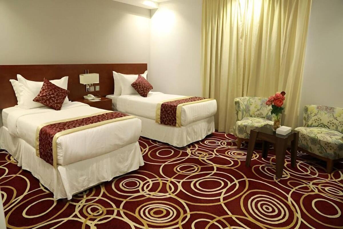 A hotel room with two beds, a desk, a chair, and a large window with curtains.