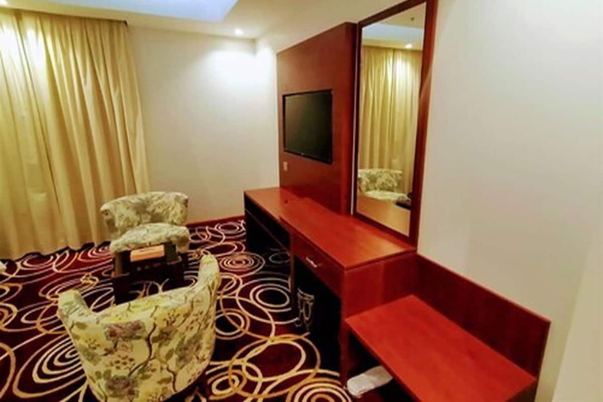 A hotel room with a large bed, a desk, a chair, a TV, and a mirror.