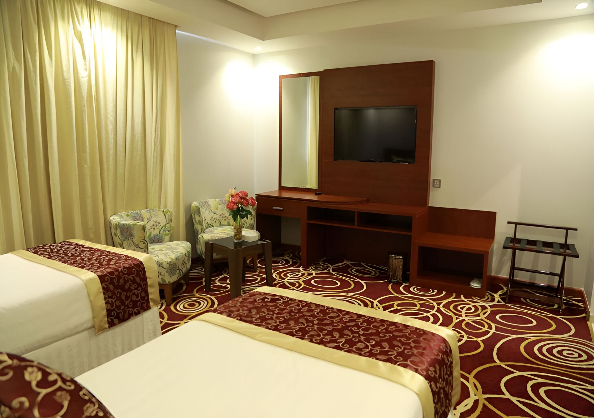 A hotel room with two beds, a TV, a desk, a chair, and a decorative vase.