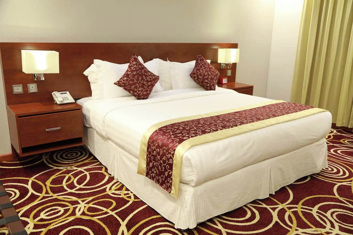 A hotel room with a large bed, two bedside tables, a telephone, and a patterned carpet.