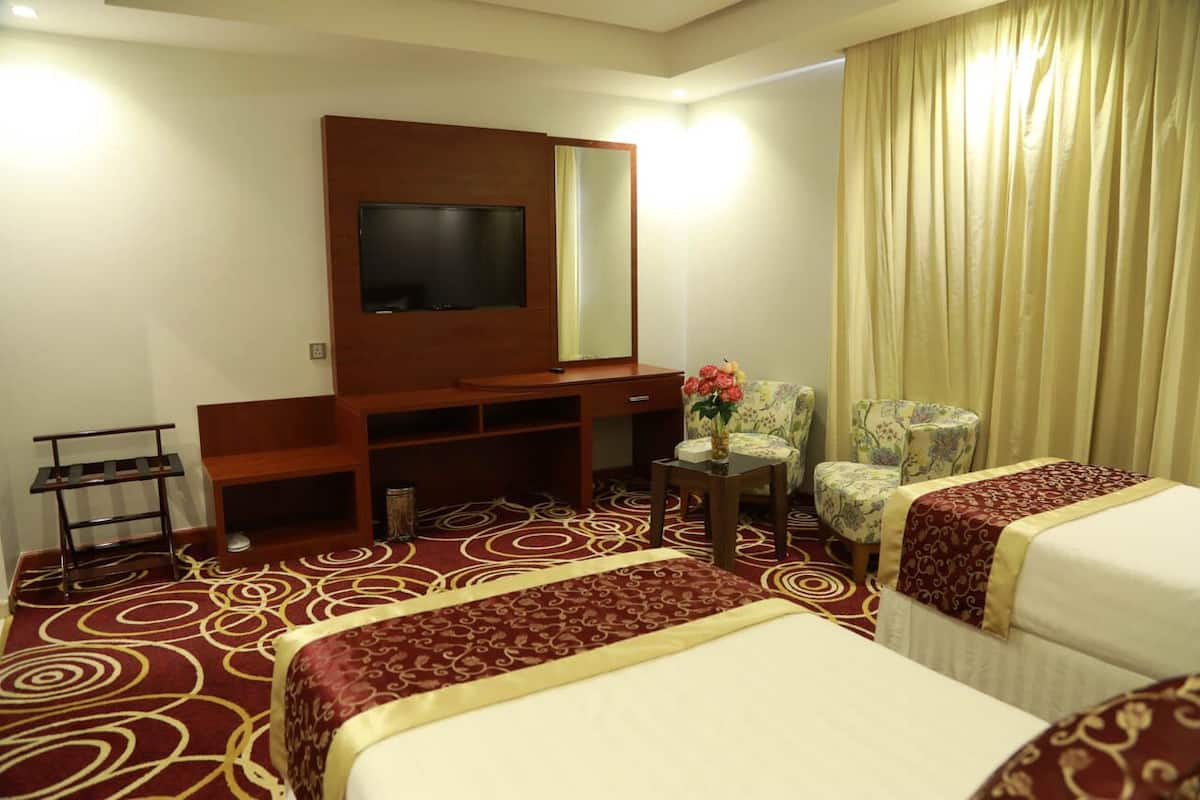 A hotel room with two beds, a TV, a mirror, a small table with a vase, and a chair.