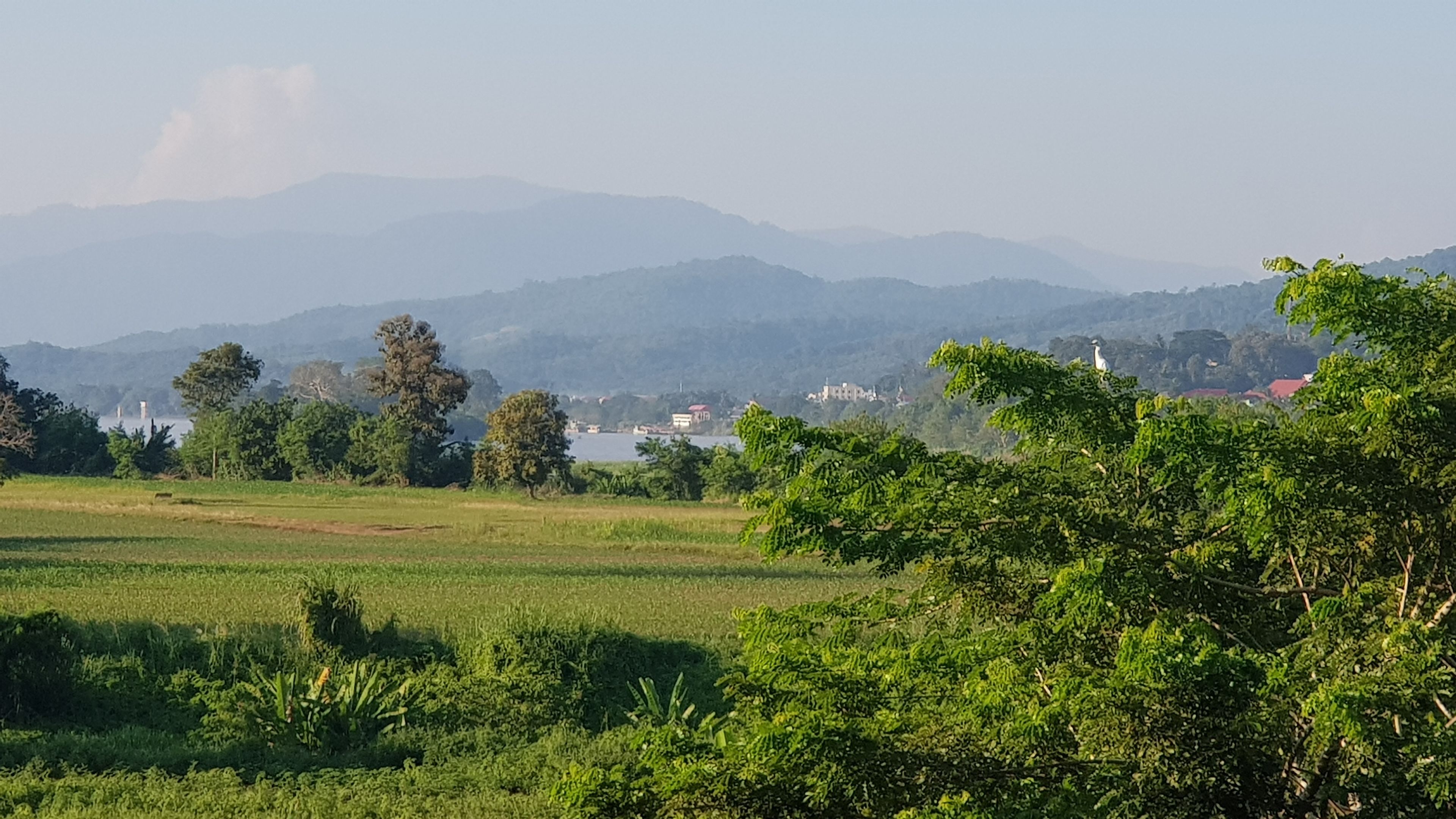 A rural landscape with fields, trees, and distant mountains.