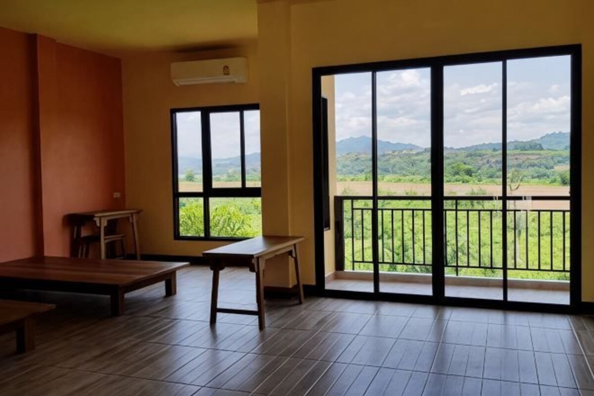 Una habitación con un amplio ventanal corredera, un banco de madera, una mesita y vistas a campos verdes y colinas.
