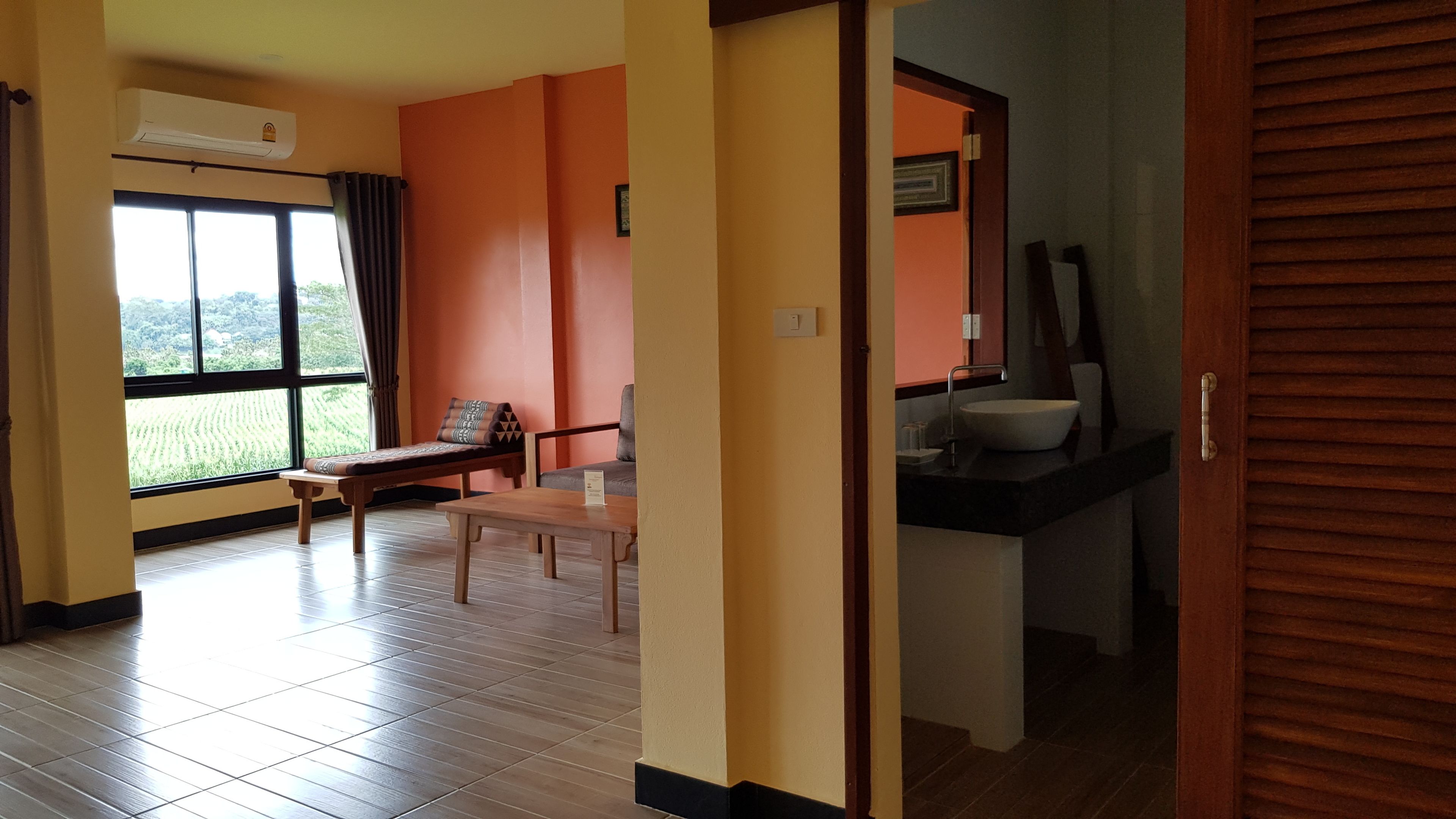 Quarto com cama, mesa, cadeira e vista para um campo verde através de uma grande janela.