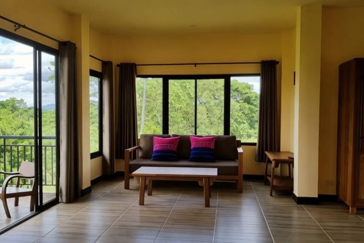 Una habitación con sofá, una mesa y vistas a la vegetación a través de amplios ventanales.