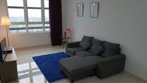 A modern living room with a grey sofa, a blue rug, a small side table with a vase of pink flowers, and a TV on a wooden stand.