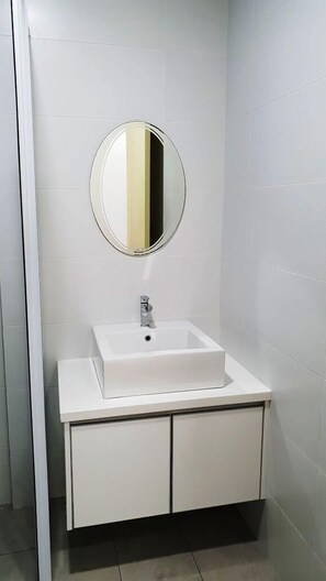 Un bagno con un lavandino bianco, uno specchio rotondo e un armadietto.