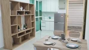 A modern kitchen with white cabinets, a wooden dining table set with plates, cups, and cutlery, and a wooden shelving unit with wine bottles.