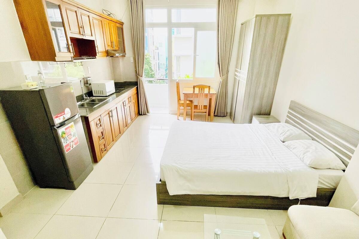 A modern hotel room with a kitchenette, a bed, a sofa, and a dining area.