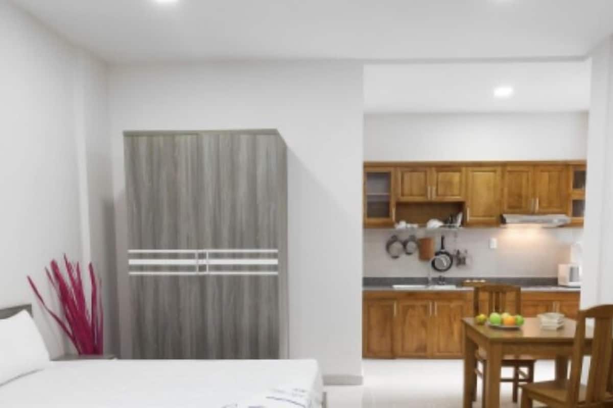 A compact hotel room with a bed, a small table with fruit, wooden cabinets, and a kitchenette.