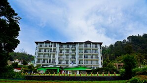 Ein mehrstöckiges Hotel mit Balkonen, umgeben von üppiger Vegetation und einem klaren Himmel.
