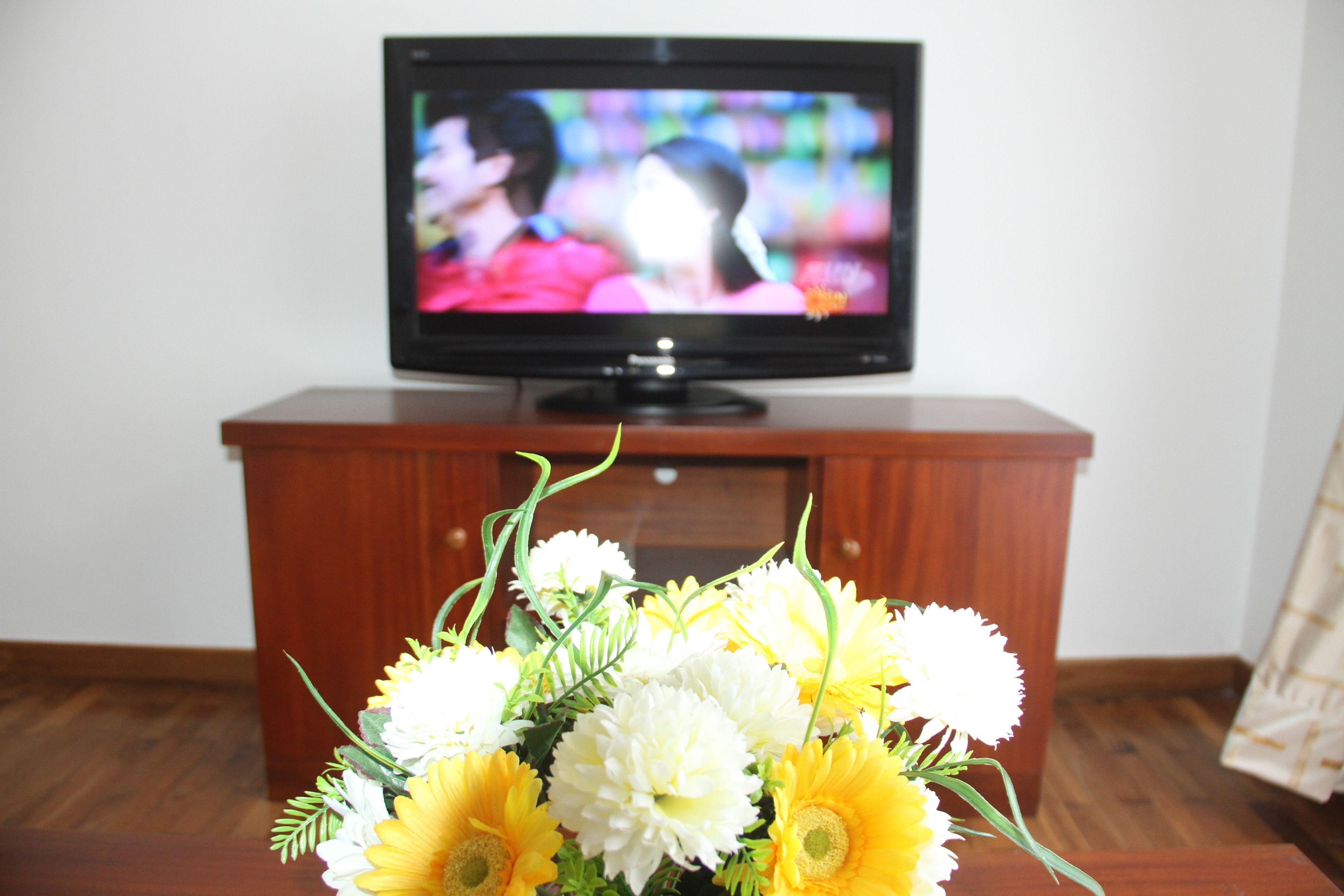 A television on a wooden cabinet with a bouquet of flowers in front.
