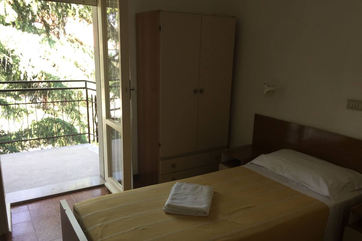 Un dormitorio con una cama, un armario de madera y un balcón con vistas a árboles.