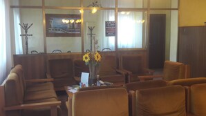 A waiting area with wooden chairs, a table with a vase of sunflowers, and a painting on the wall. - Hotel Belvedere (Castrocaro Terme)