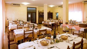 A dining hall with multiple tables set for meals, featuring white tablecloths and wooden chairs. - Hotel Belvedere (Castrocaro Terme)