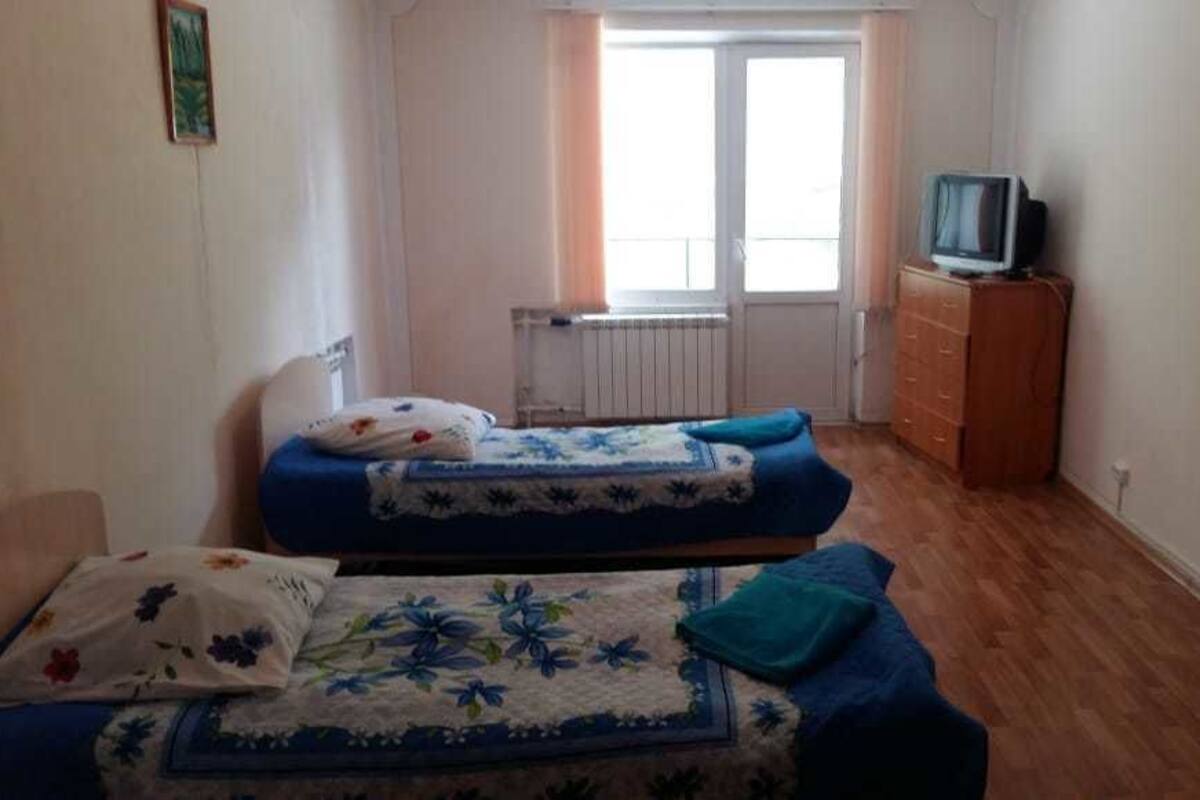 Une chambre avec deux lits, une commode, une télévision et une fenêtre.