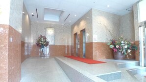A lobby with a marble floor, red carpeted steps, and a large potted plant. - Hotel Times-Inn24 Tsunashima (Yokohama)