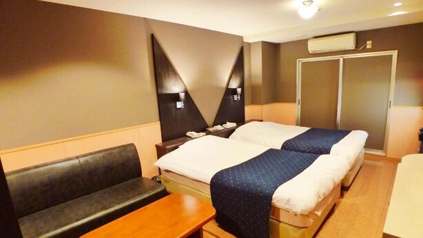 A hotel room with a bed, a bench, a bedside table, and a wardrobe. - Hotel Times-Inn24 Tsunashima (Yokohama)