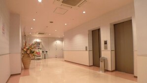 A hotel corridor with a reception desk, a trash bin, and an elevator. - Hotel Times-Inn24 Tsunashima (Yokohama)