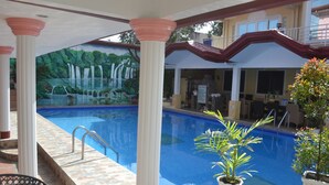 A swimming pool with a mural of a waterfall, surrounded by columns and potted plants.