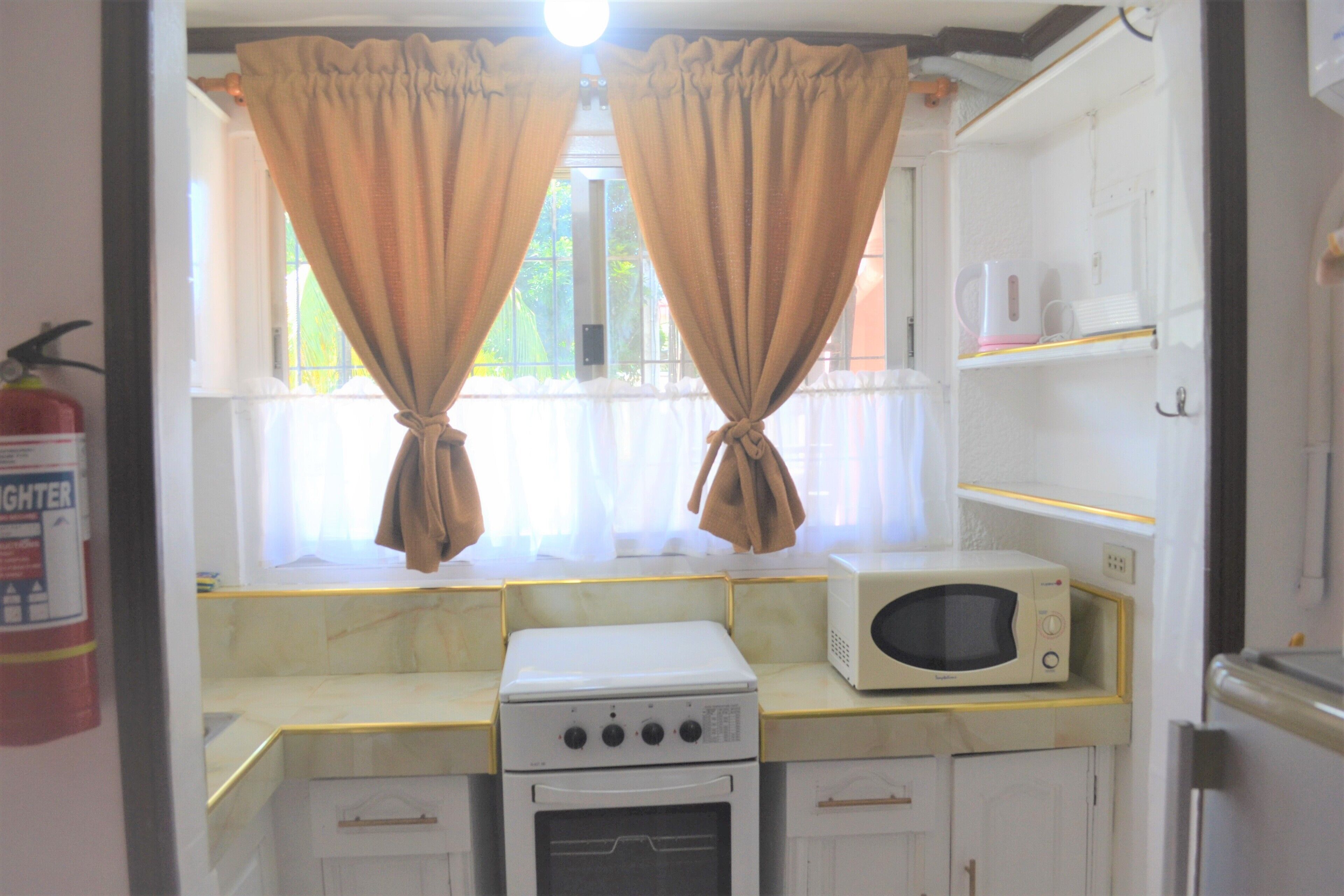 A compact kitchen with a stove, oven, microwave, and a window with curtains.
