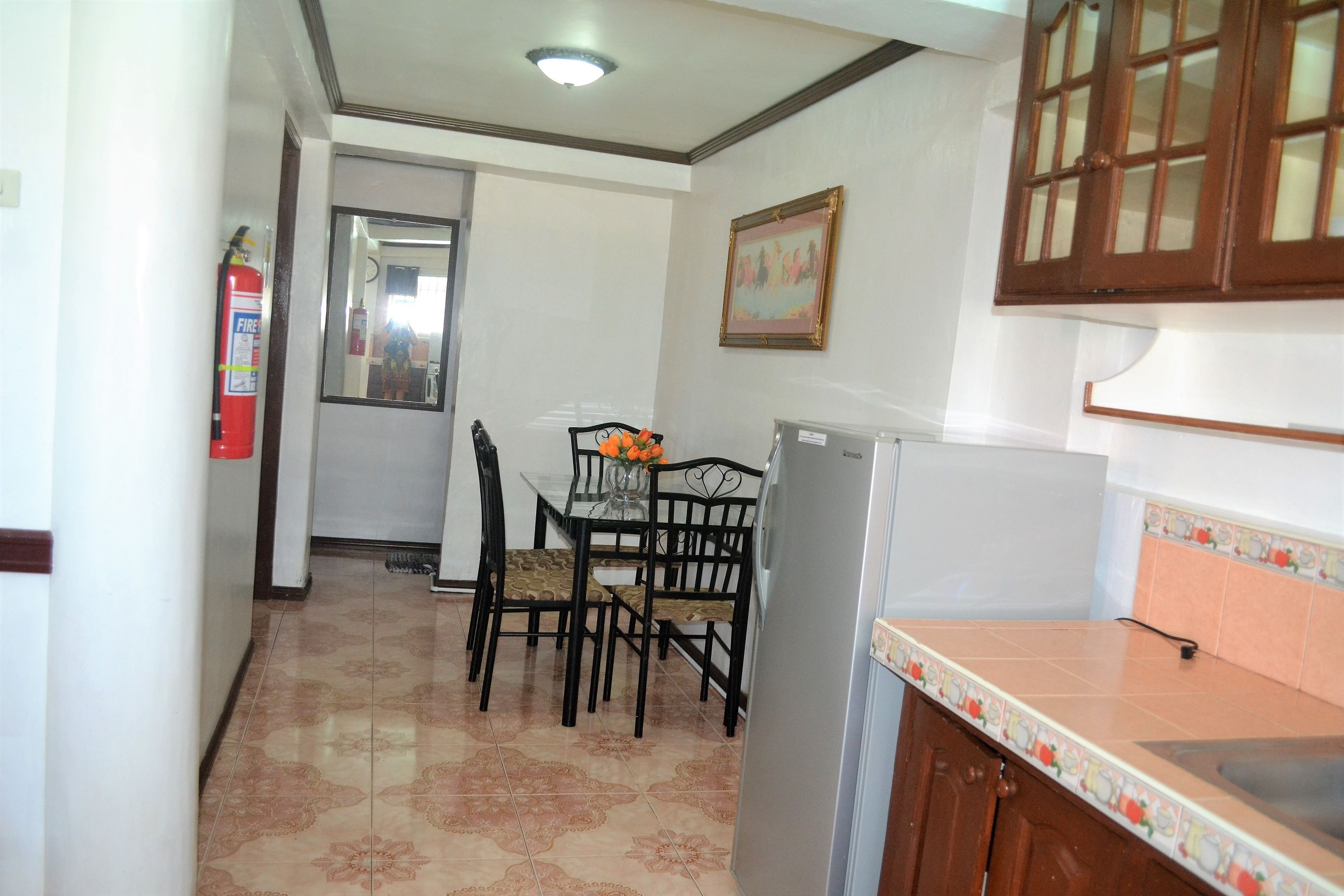 Una cocina con refrigerador, una mesa de comedor con sillas y un extintor.