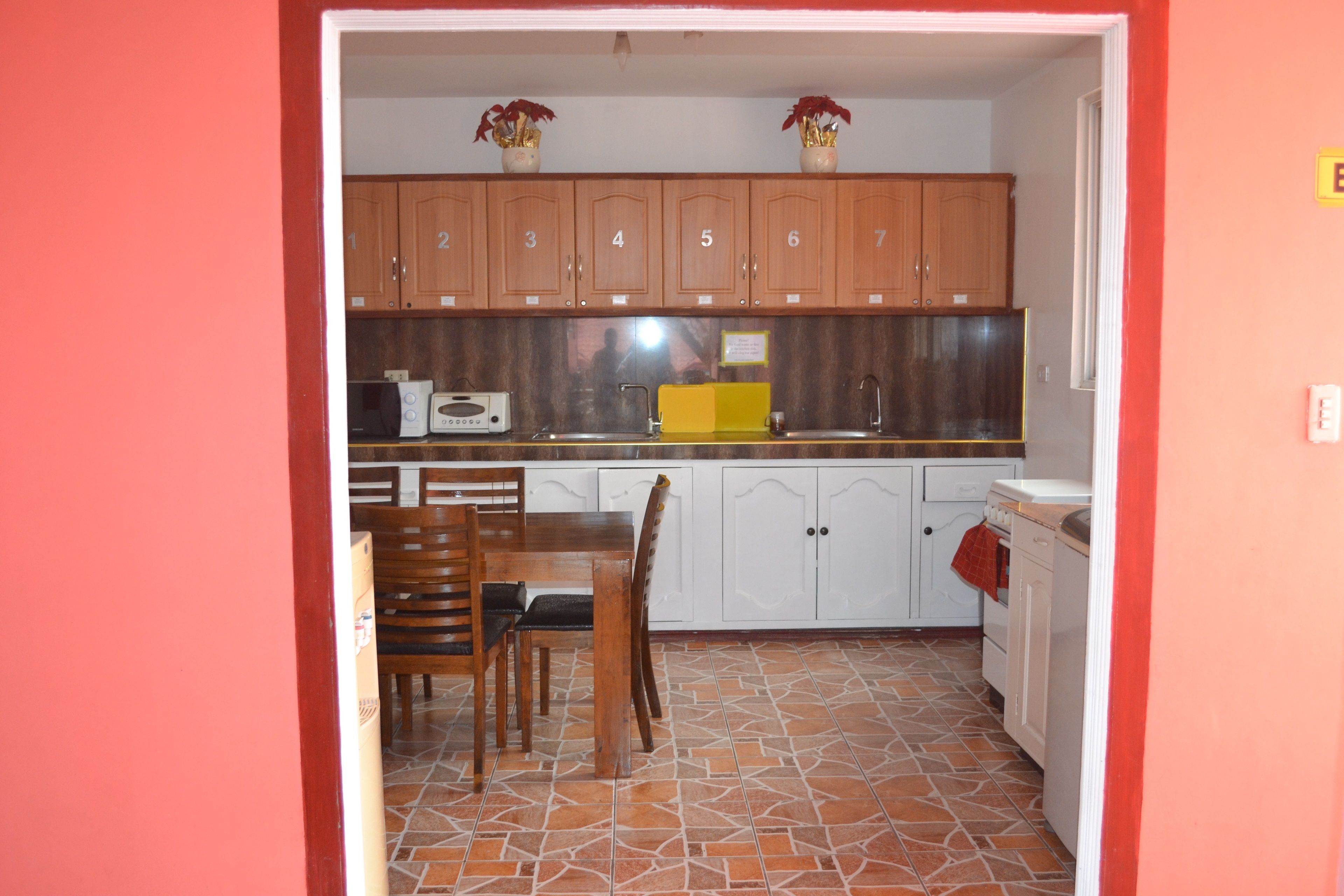 Una cocina con armarios de madera, piso de baldosas, una mesa de comedor con sillas y un microondas.