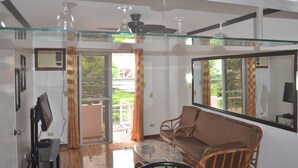 A living room with a glass coffee table, a sofa, a television, and a ceiling fan.