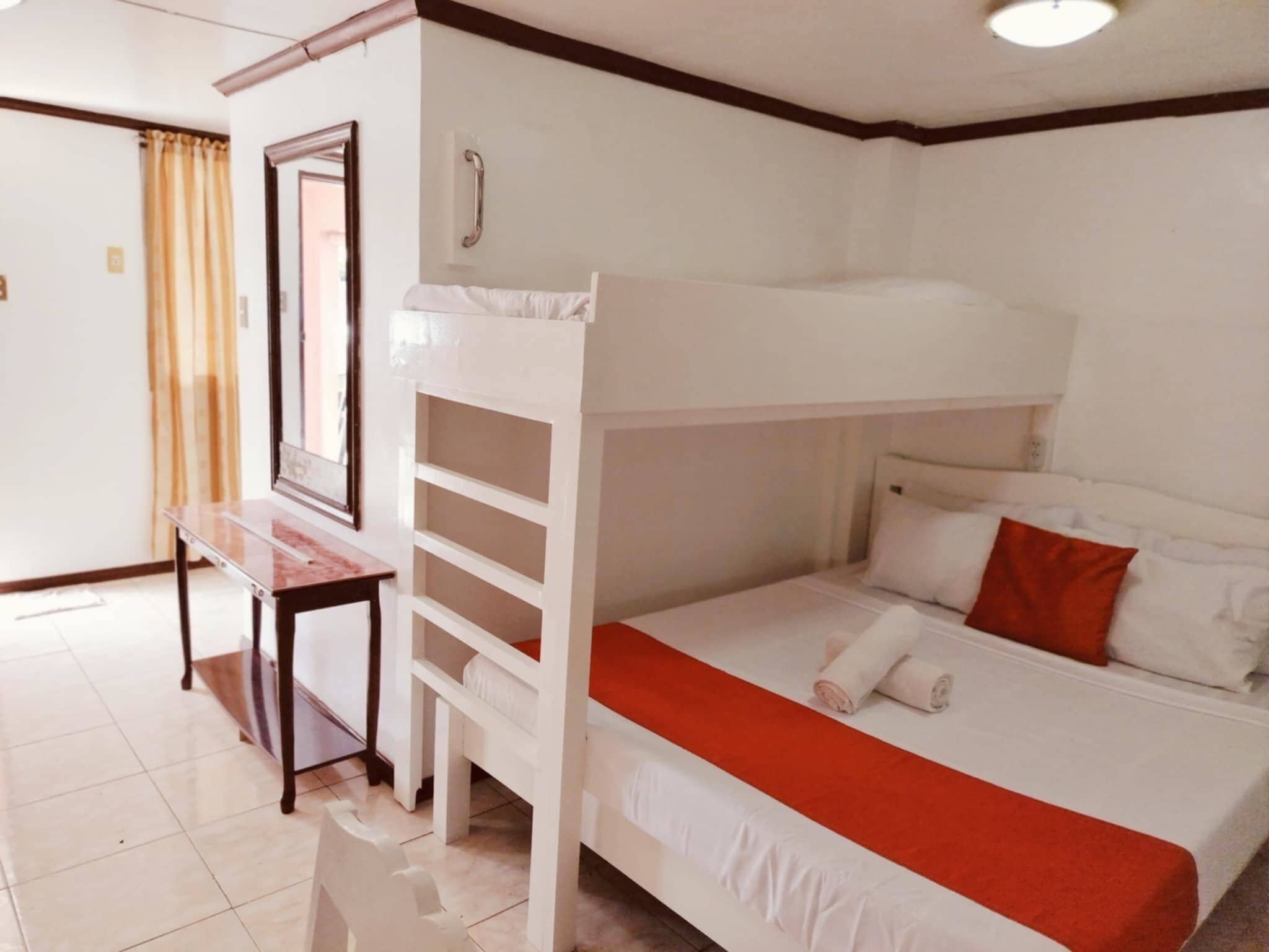 A bunk bed with a desk and shelves, a mirror, and a red pillow.