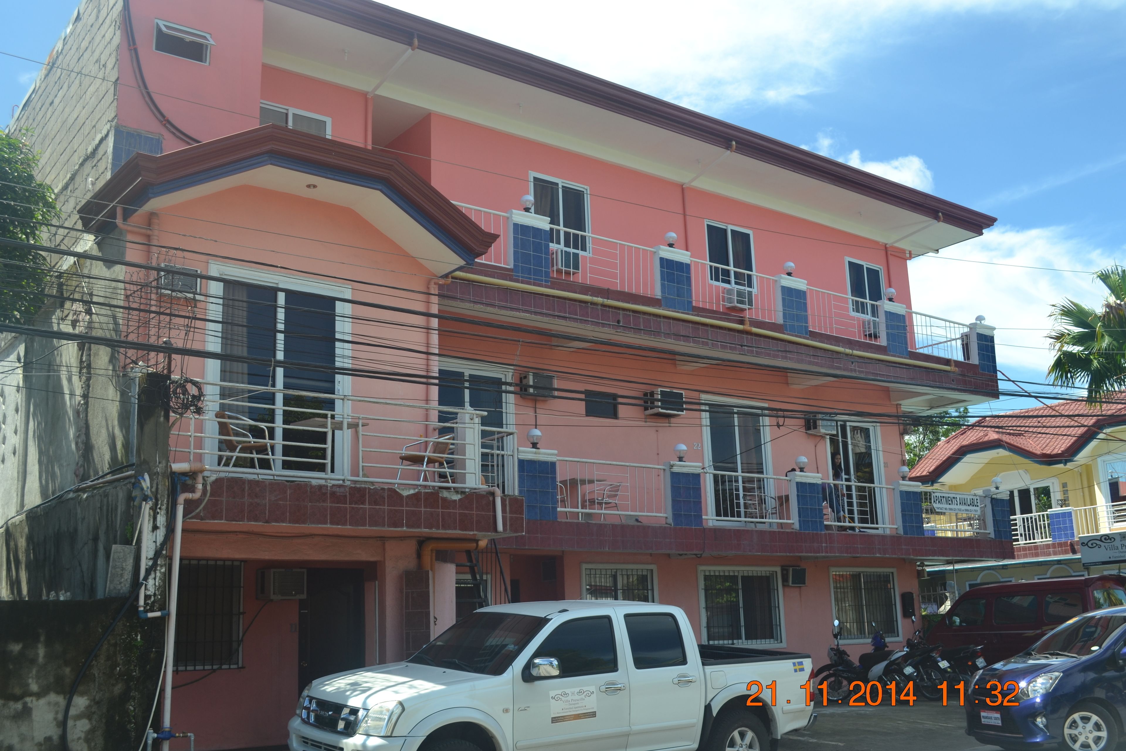 A two-story building with balconies, a white pickup truck parked in front, and a date stamp of 21.11.2014 11:32.