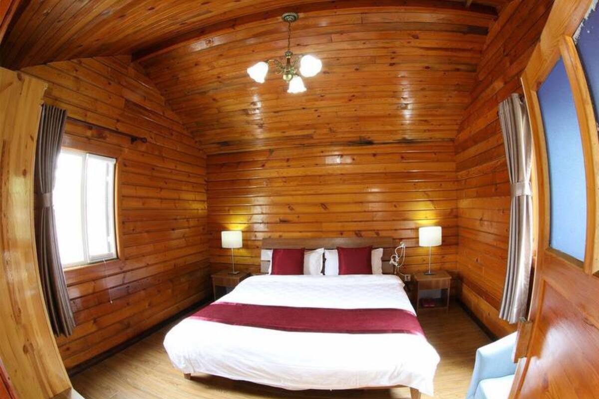 A wooden cabin bedroom with a bed, two bedside lamps, and a window.