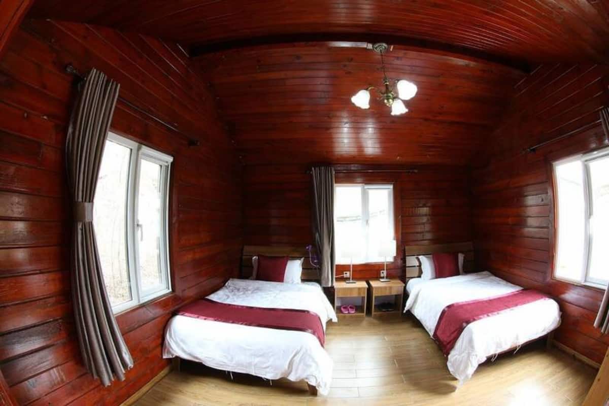 A cabin with two beds, wooden walls, a wooden floor, and a window with curtains.