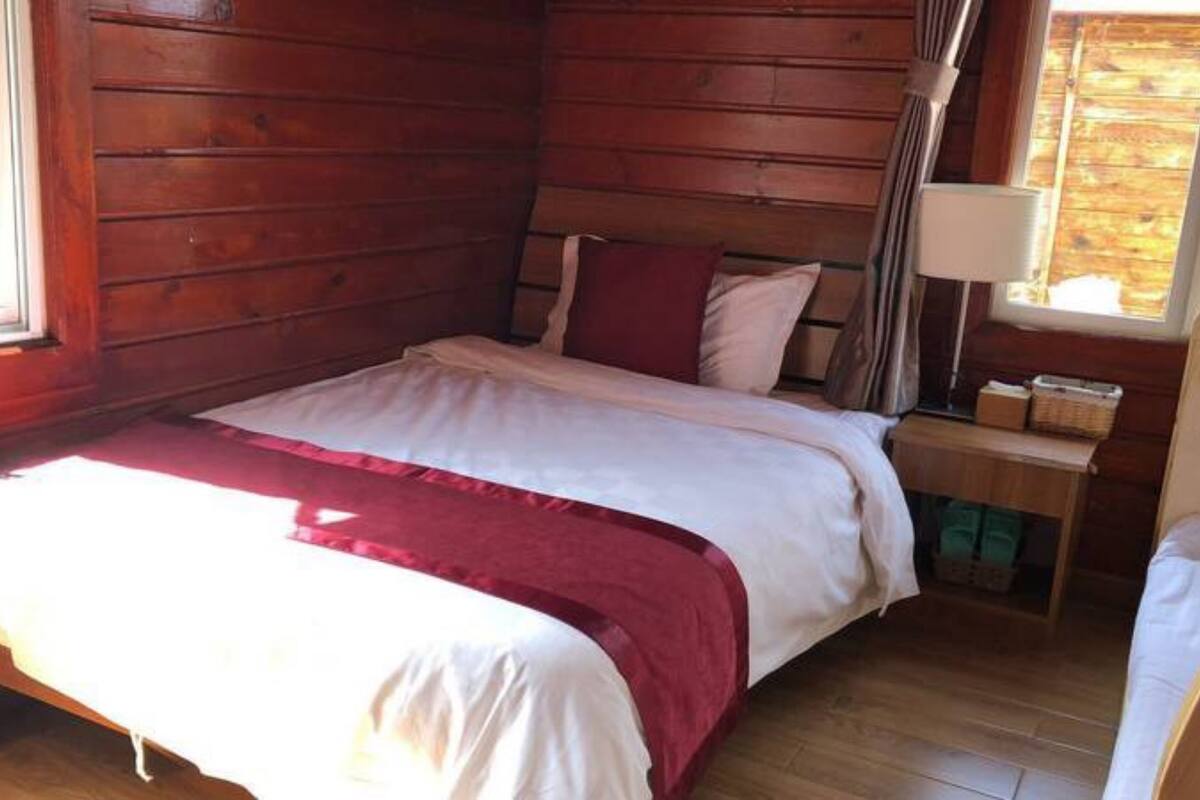 A wooden cabin bedroom with a bed, pillows, a nightstand, and a window.