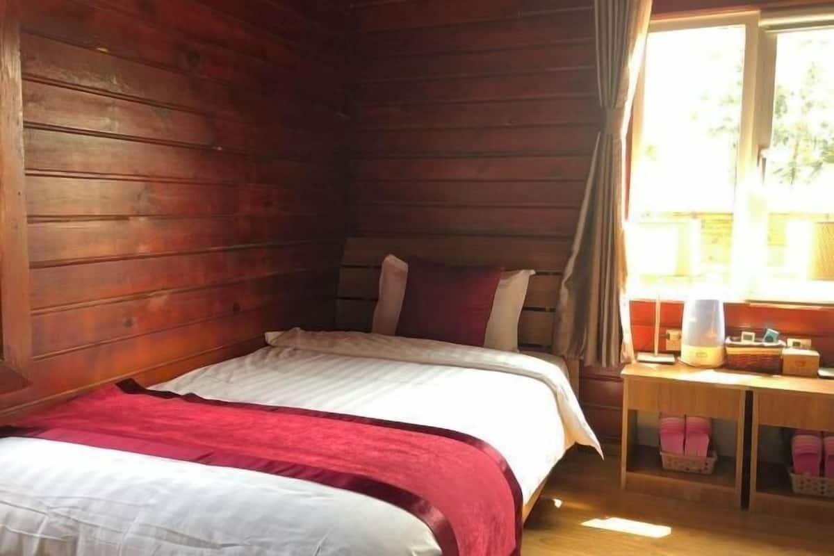 A wooden cabin room with a bed, a small table, and a window.