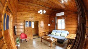 Ein rustikales Blockhaus-Interieur mit Holzbalkendecke, einer Couch, einem roten Sessel und einem Tisch.