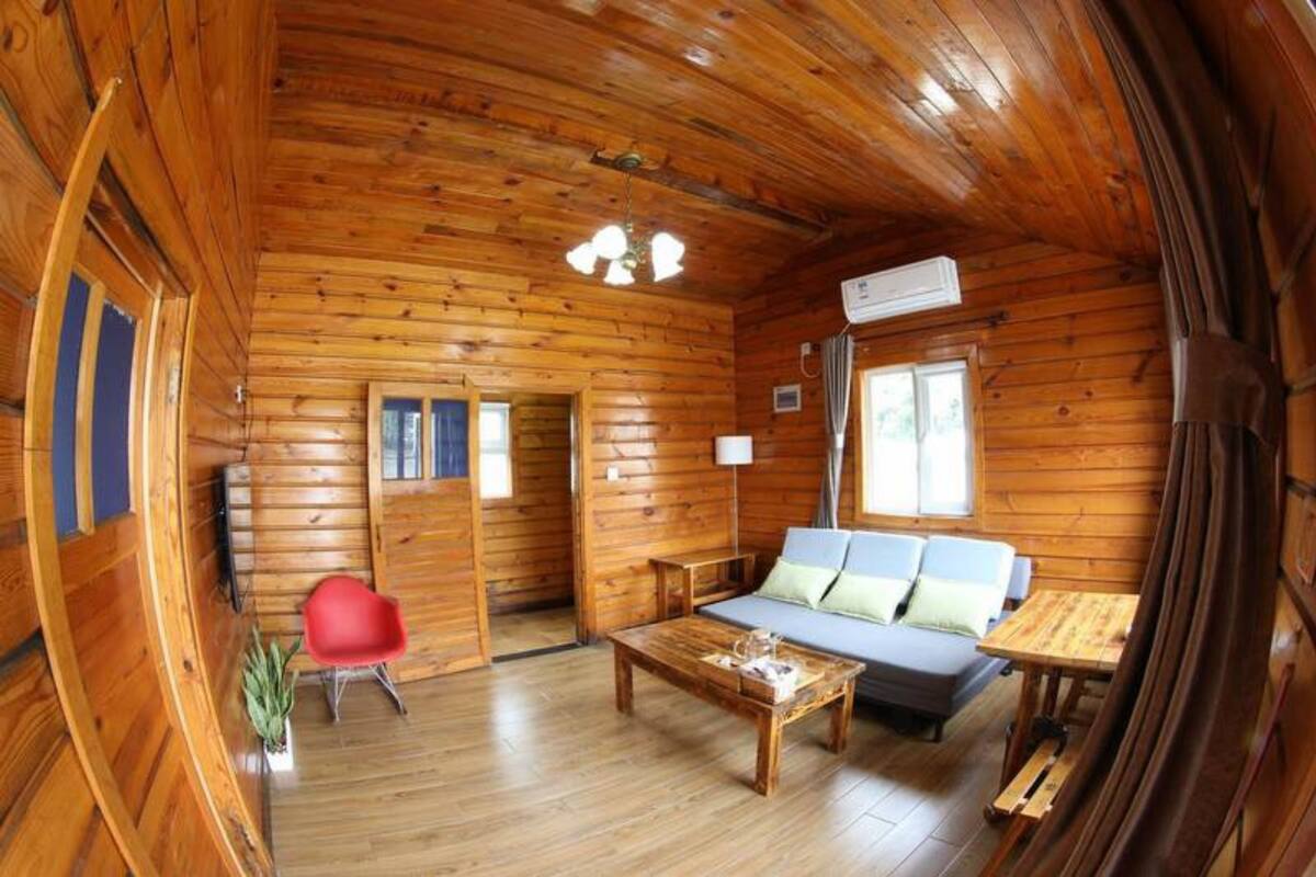 A log cabin interior with a wooden ceiling, a sofa, a red chair, and a table.