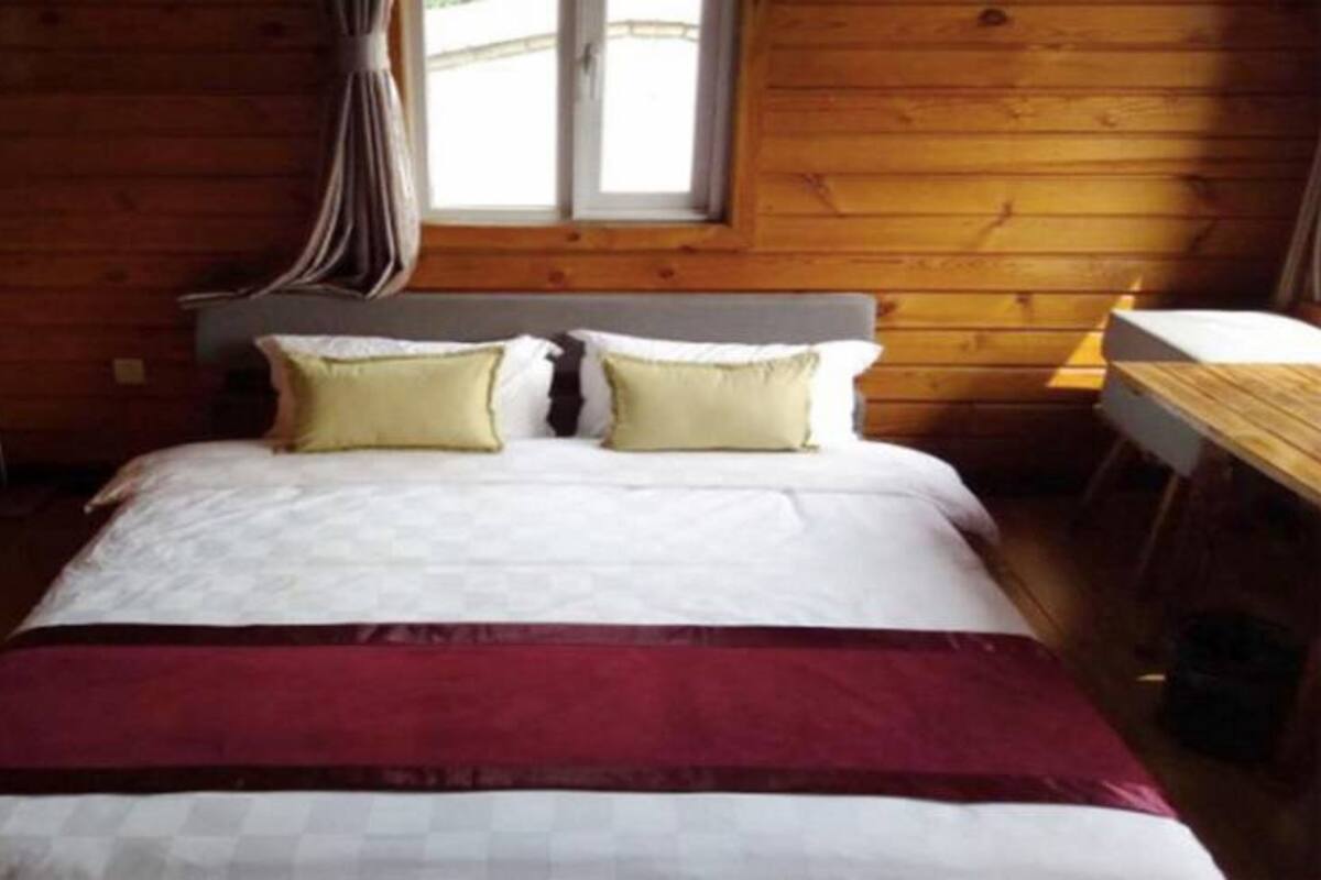 A wooden cabin room with a bed, two pillows, a nightstand, and a window with curtains.