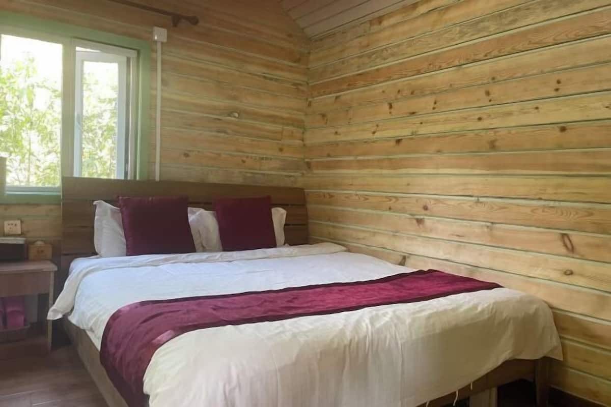 A wooden cabin room with a bed, pillows, a nightstand, and a window.