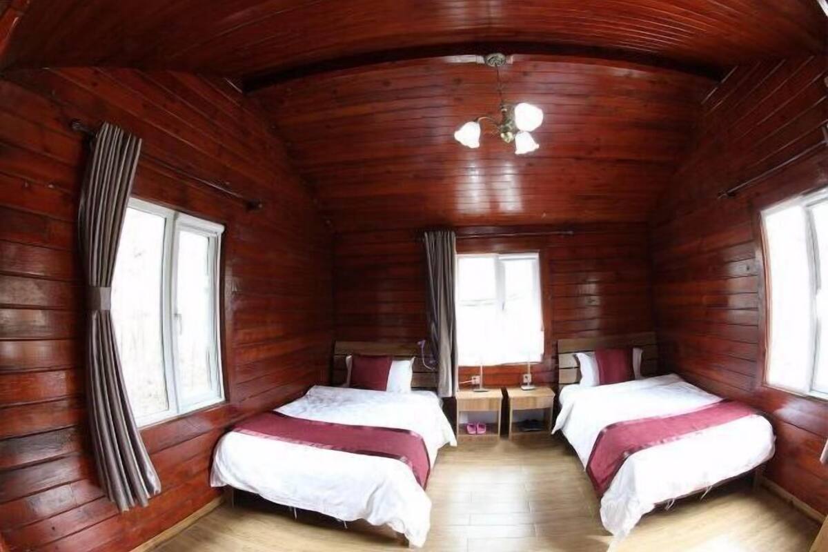 A cabin with two beds, wooden walls, a ceiling fan, and a window.