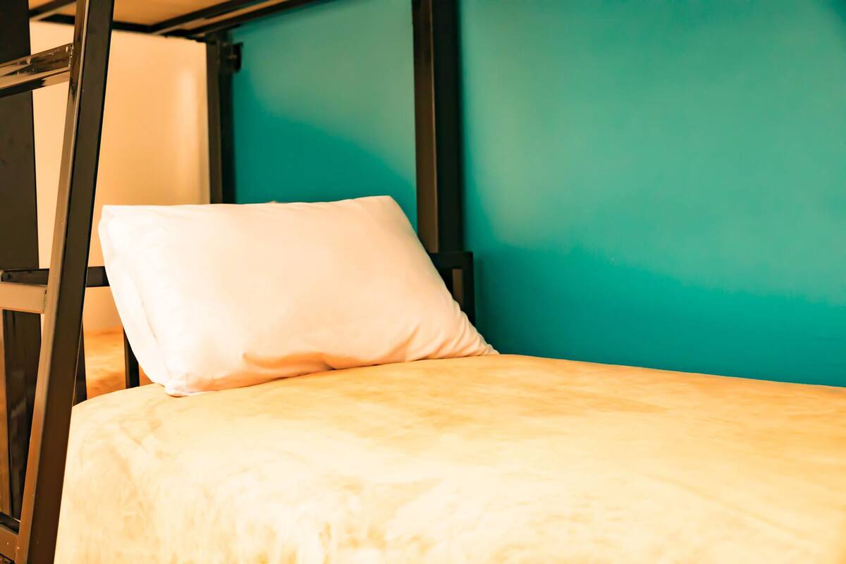 Un lit superposé avec un oreiller blanc et un matelas beige, adossé à un mur de couleur turquoise.