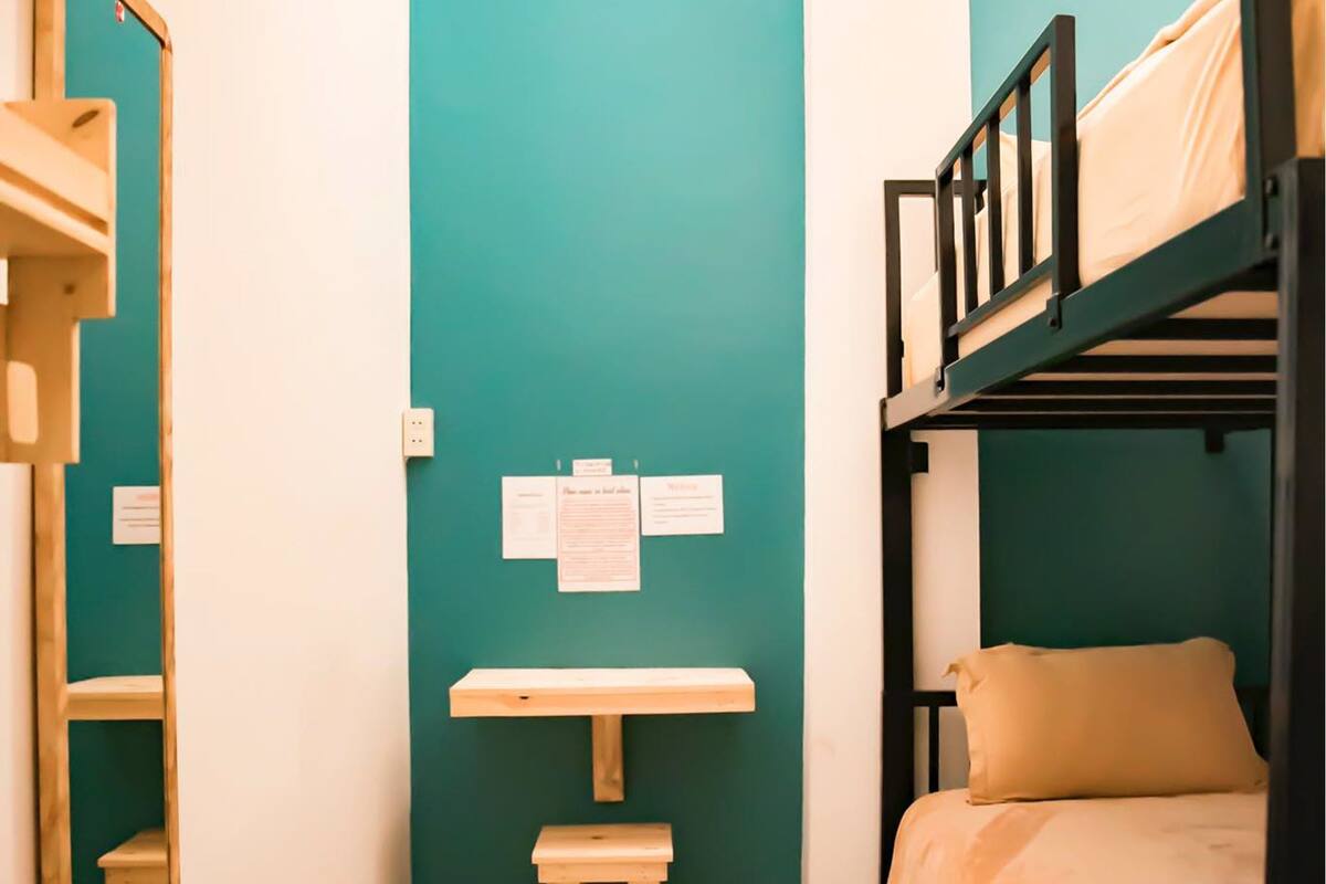 Une chambre de dortoir avec un lit superposé, un bureau avec une chaise, un miroir et un mur de couleur turquoise.