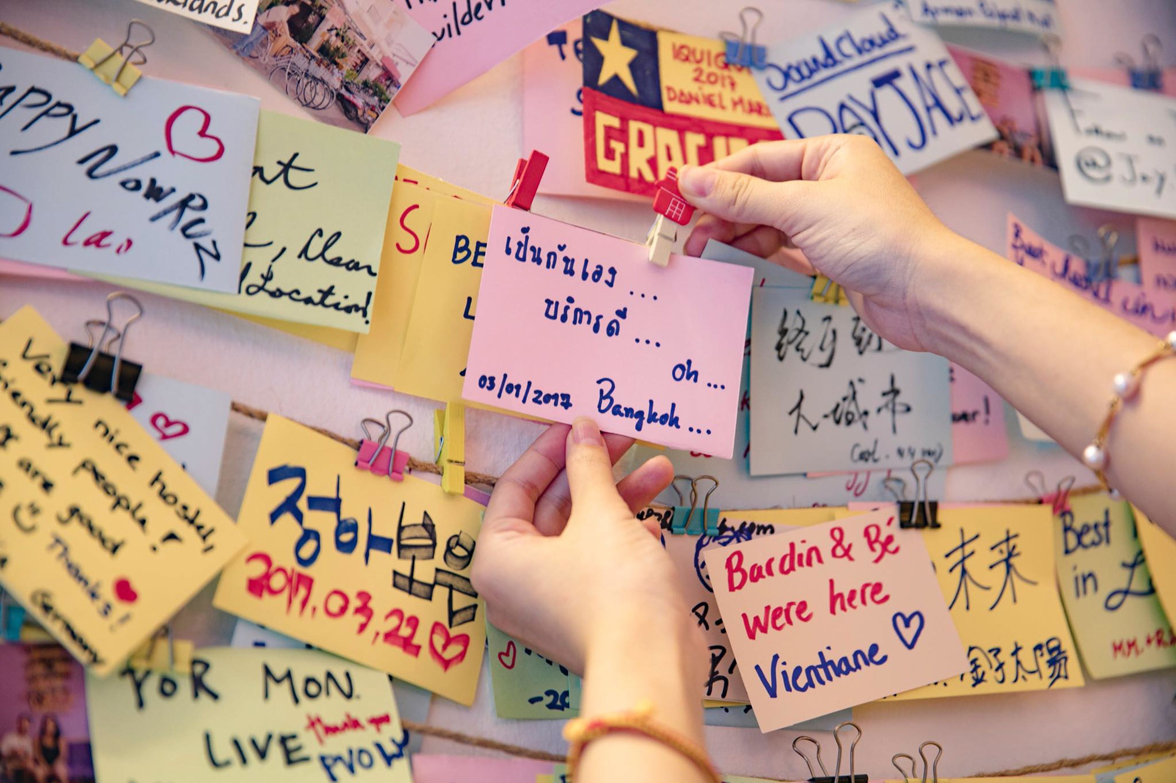 A wall covered with colorful sticky notes and handwritten messages, some clipped with binder clips.