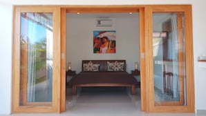 A bedroom with a bed, a painting on the wall, and a sliding glass door leading to another room. - Fabia Villas (Seminyak)