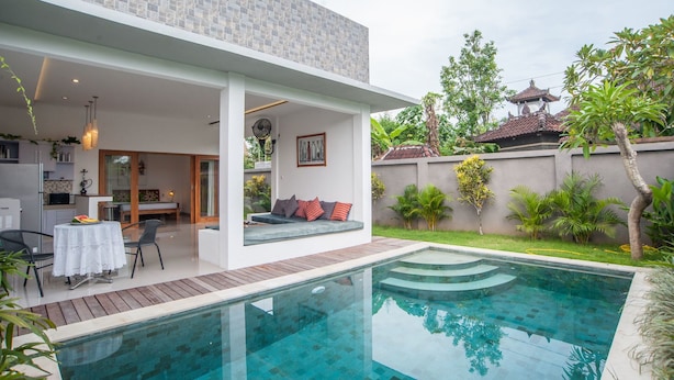 A modern house with a swimming pool, a patio with a table and chairs, and a garden with various plants. - Fabia Villas (Seminyak)