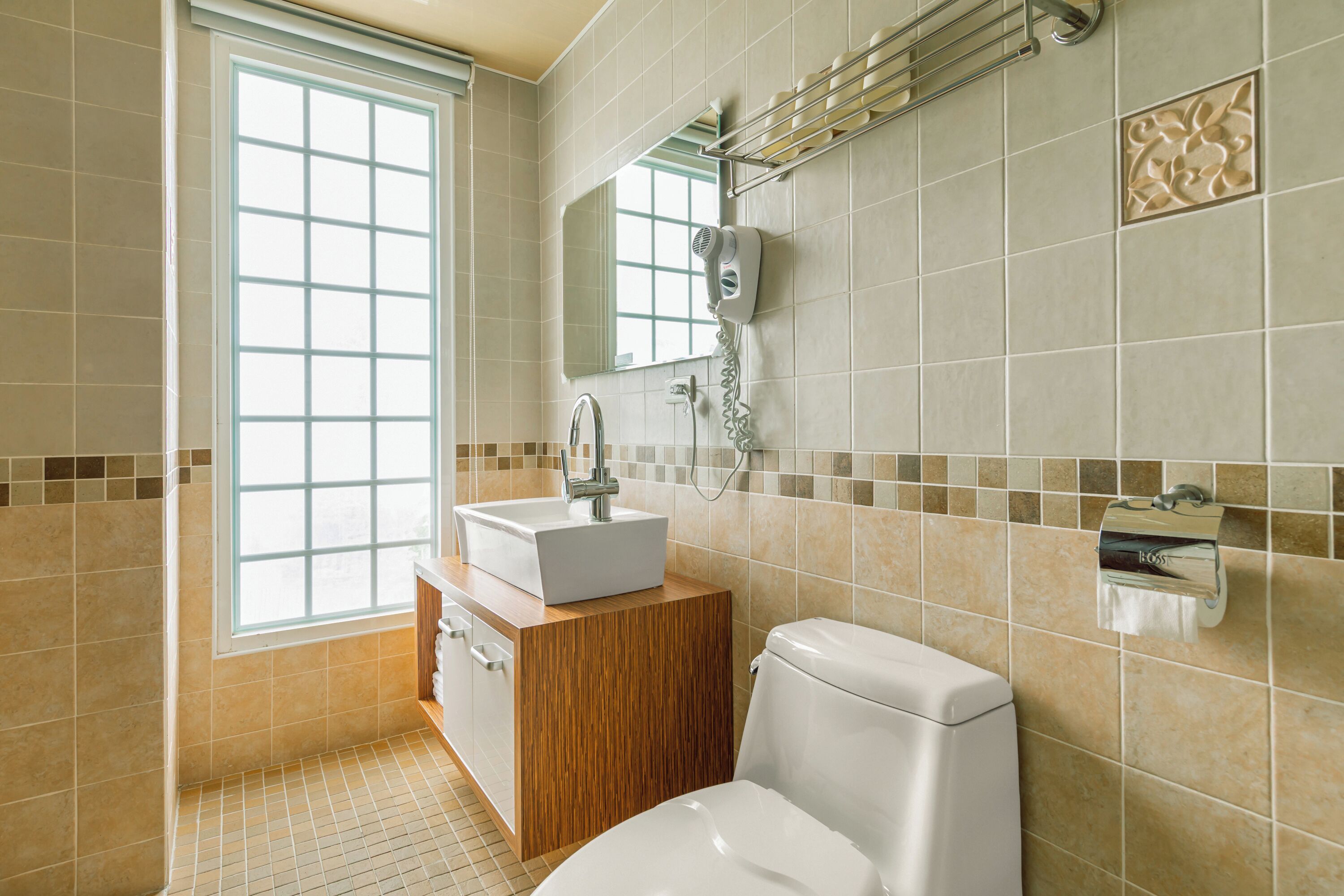 Un baño con ventana, lavamanos, inodoro y dispensador de toallas.