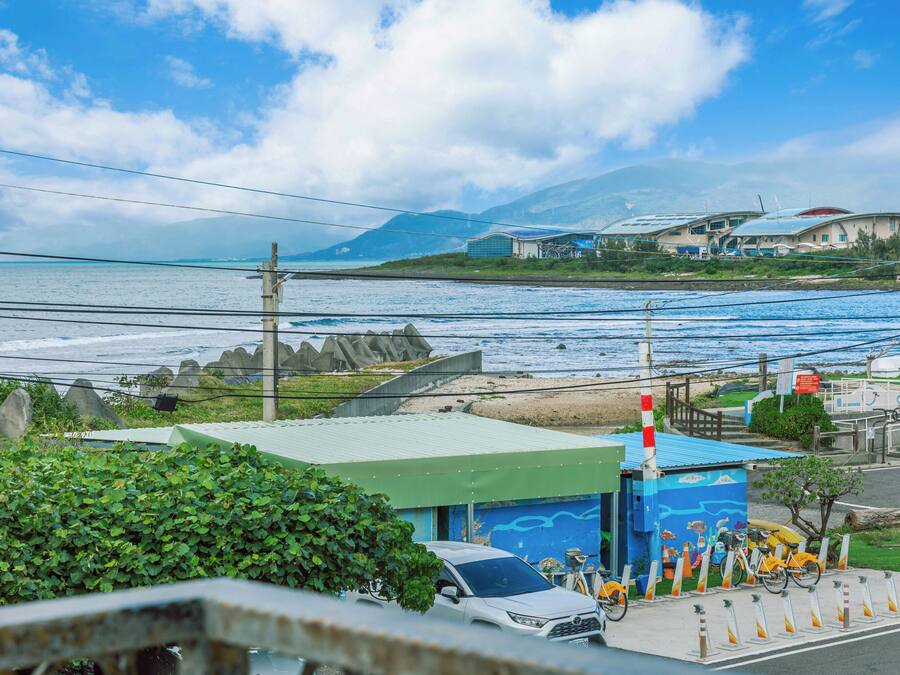 A coastal view with a building featuring a green roof and a mural, a parked car, and a bicycle.